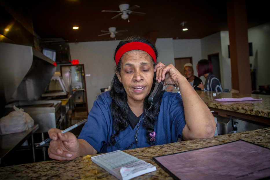 An African American woman listens to a takeout order on the phone in a restaurant.