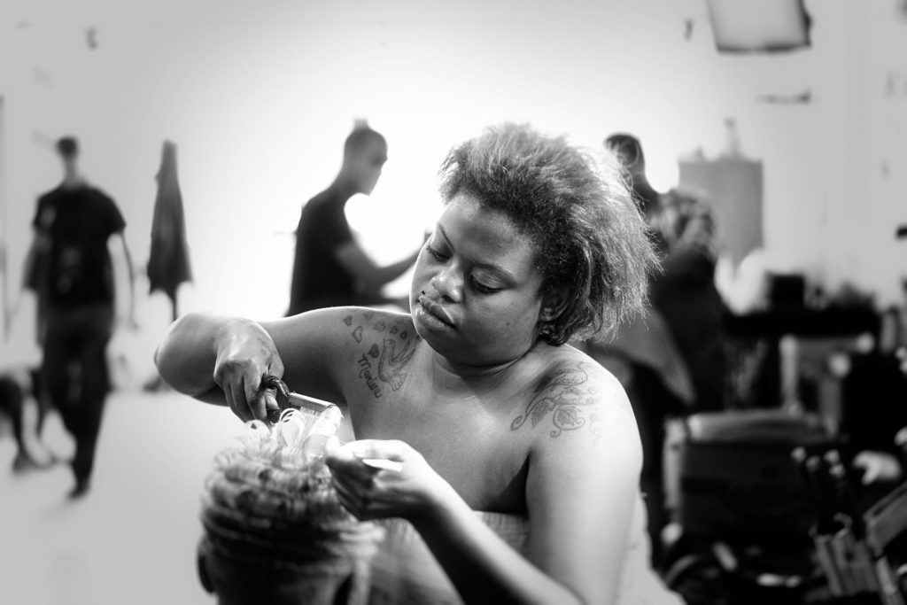 An African American woman with short hair and tattoos on her shoulders cuts a woman's hair in a salon.