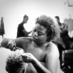 An African American woman with short hair and tattoos on her shoulders cuts a woman's hair in a salon.