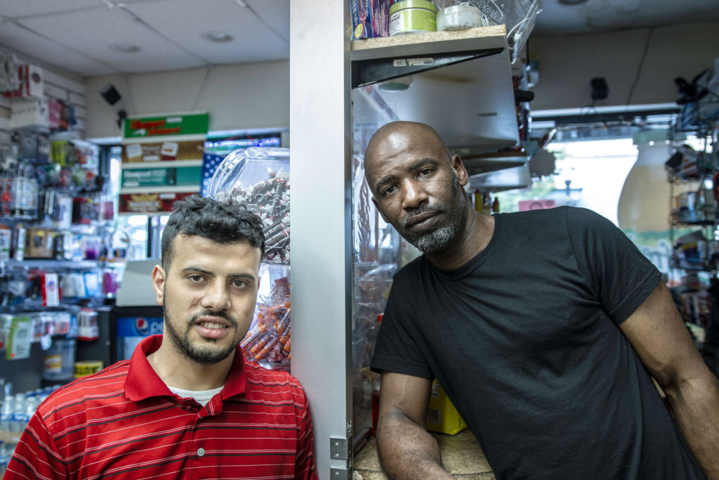 Two men smile as they stand in a stores that sells candy and Pepsi products.