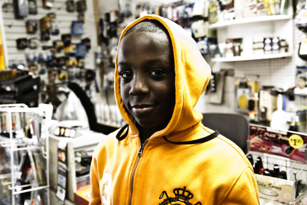 An African American boy wears a bright yellow hooded sweatshirt as he smiles in a store environment.