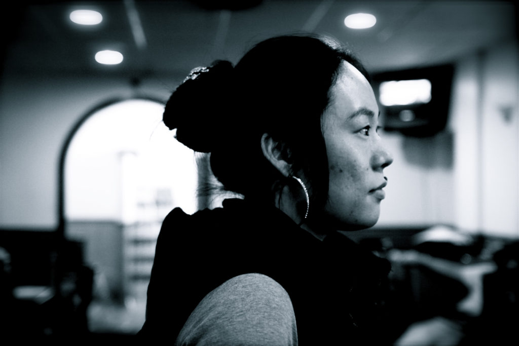An Asian American woman with her hair in a bun and large hoops earrings looks off to the side.