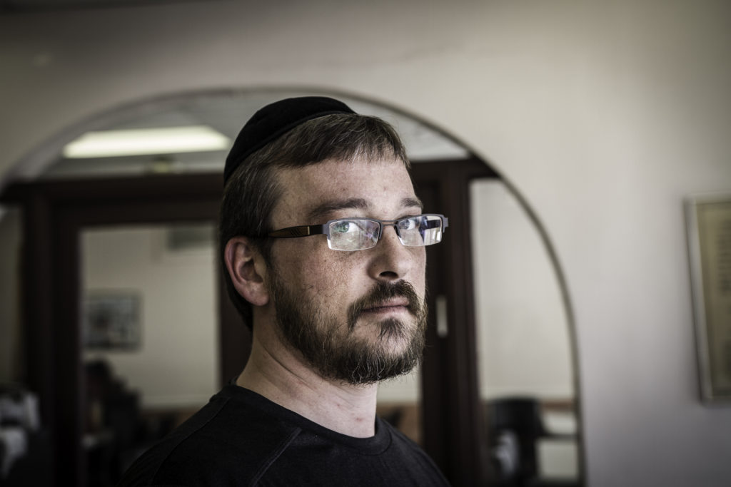 A white man in a black yamaka cap and eyeglasses in a home setting.