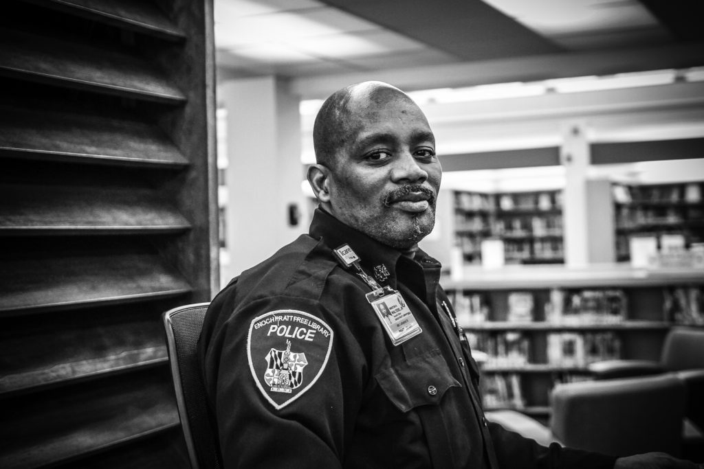 An African American police officer smiles at the camera in a library setting.