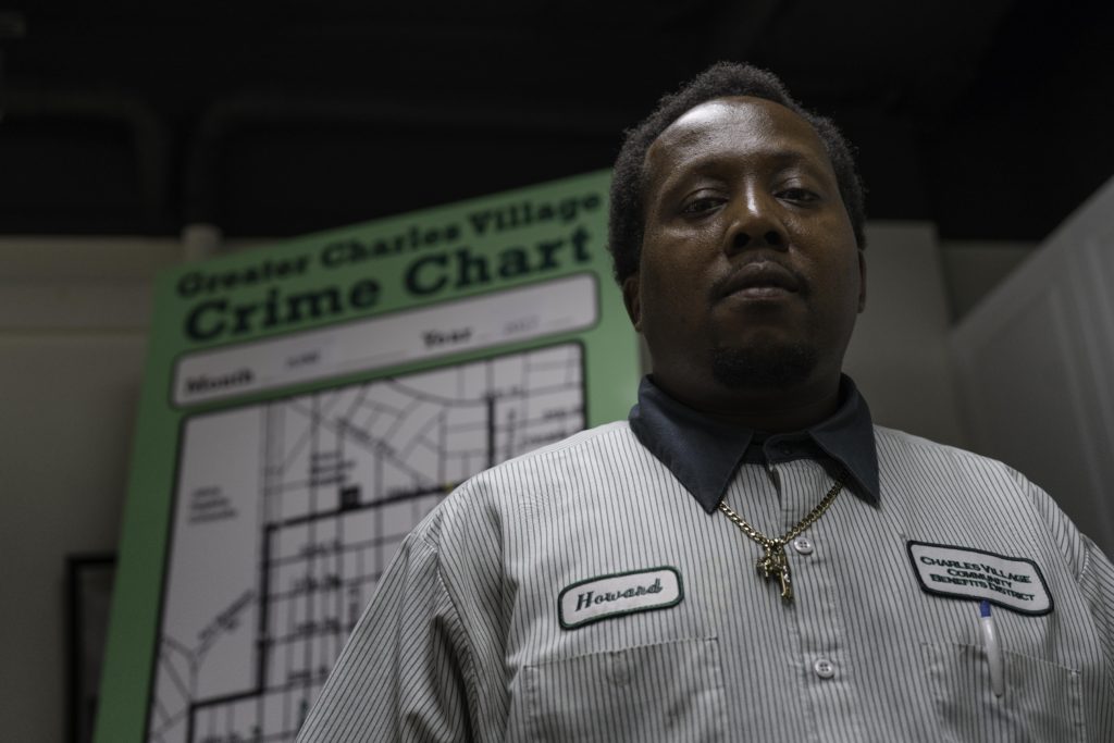 An African American man with a gray, striped shirt and a gold necklace stands in front of a map that reads, Crime Chart.
