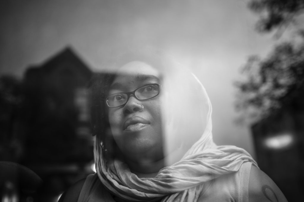 A woman with a head scarf looks at the window in a black-and-white photo.
