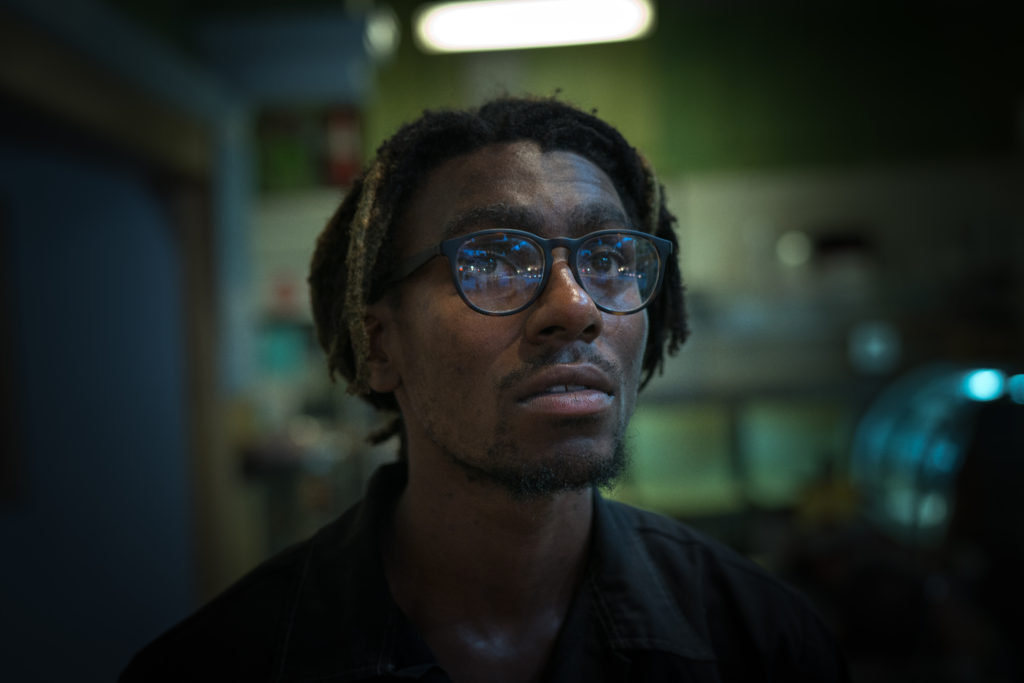 An African American man with broad, circular framed glasses looks up pensively. 