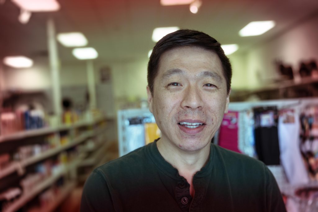 A light-skinned man with a black shirt stands in a hair supply store.