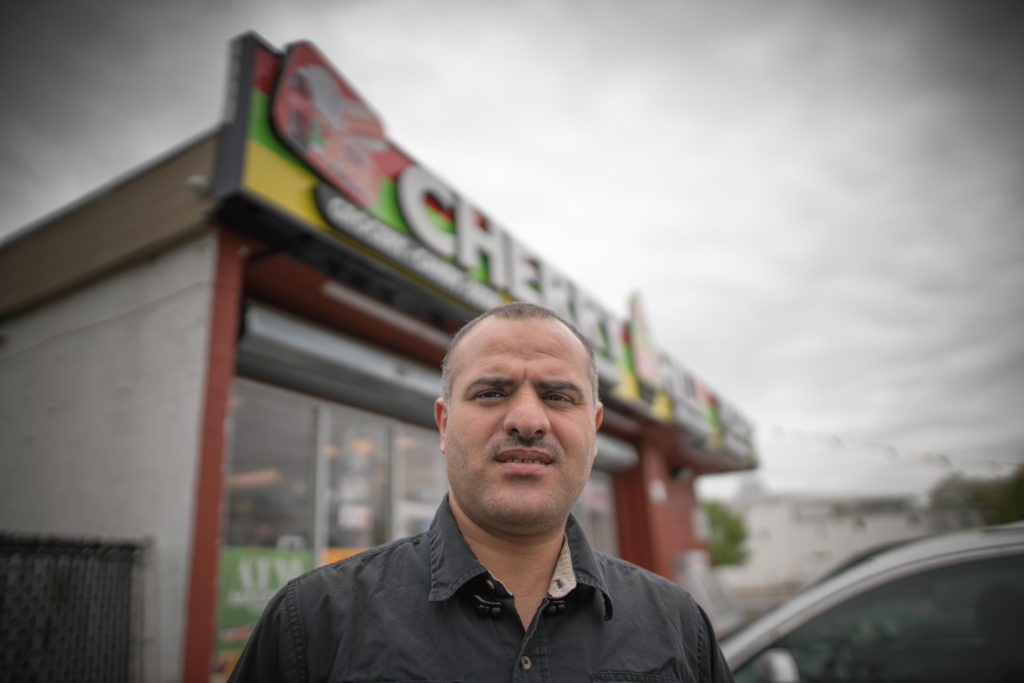 A light-skinned man with short cropped hair stands outside in front of the Cherry Hill Mart.